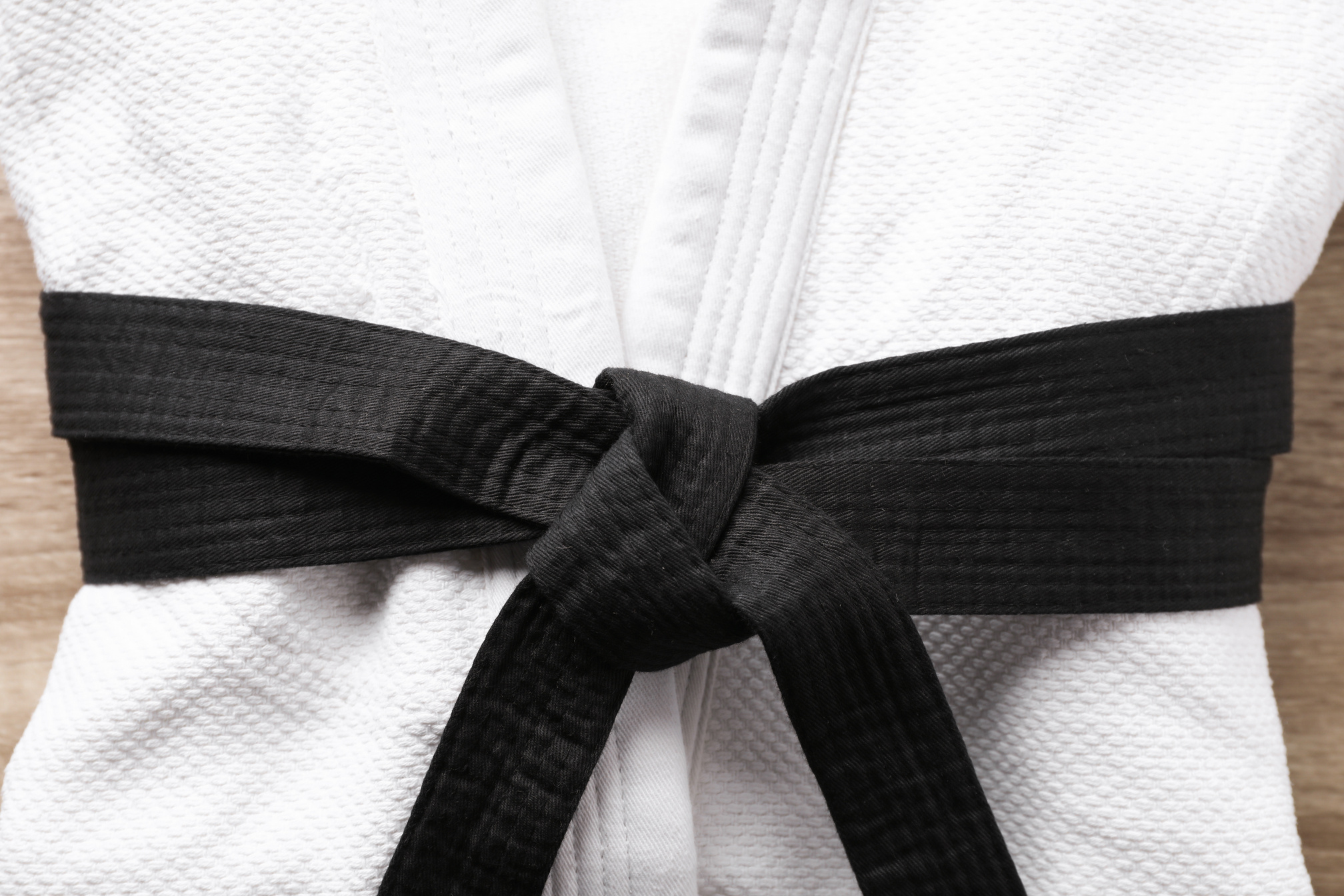 Martial Arts Uniform with Black Belt on White Wooden Background, Closeup